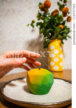 Sweet dessert in the form of a yellow green apple on a plate. A sweet treat in a pastry shop, cafeteria and female hand. Take the baked apple pie. Sweet dessert in the form of a yellow green apple on a plate. A sweet treat in a pastry shop, cafeteria and female hand. Take the baked apple pie. 119747381