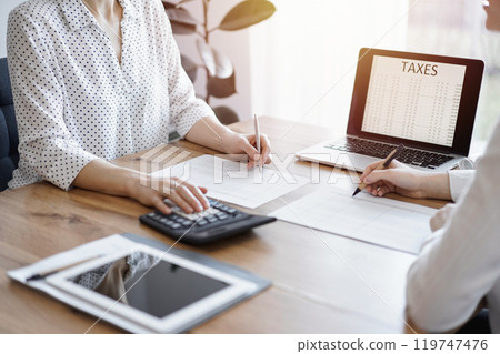 Two accountants using a laptop computer and calculator while counting taxes at wooden desk in office. Teamwork in business audit and finance 119747476