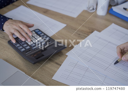 Accountants or auditors reviewing financial documents while using laptop, calculator and sitting opposite one another at the wooden desk in office, view above. Audit and taxes Accountants or auditors reviewing financial documents while using laptop, calculator and sitting opposite one another at the wooden desk in office, view above. Audit and taxes 119747480