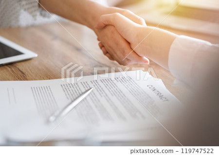 Business people shaking hands above contract papers just signed on the wooden table, close up. Lawyers at meeting. Teamwork, partnership, success concept Business people shaking hands above contract papers just signed on the wooden table, close up. Lawyers at meeting. Teamwork, partnership, success concept 119747522