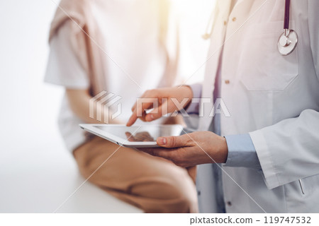Doctor and patient in clinic. Friendly physician using tablet computer near a young woman. Medicine concept Doctor and patient in clinic. Friendly physician using tablet computer near a young woman. Medicine concept 119747532