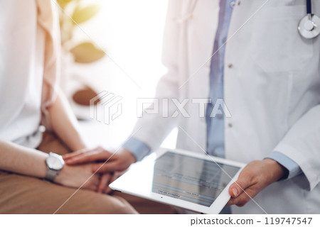 Doctor and patient discussing health exam results. Friendly physician reassuring a young woman by one hand while keeping tablet computer in another. Medicine concept Doctor and patient discussing health exam results. Friendly physician reassuring a young woman by one hand while keeping tablet computer in another. Medicine concept 119747547