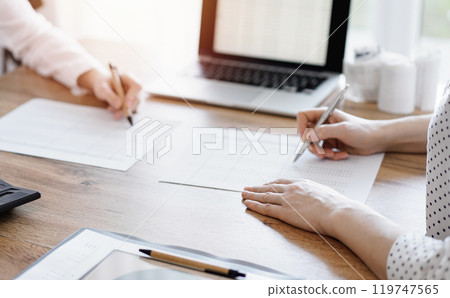 Two accountants using a laptop computer and calculator while counting taxes at wooden desk in office. Teamwork in business audit and finance 119747565