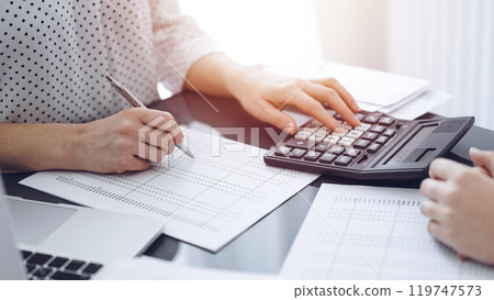 Woman accountant using a calculator and laptop computer while counting taxes with a client or a colleague. Business audit team, finance advisor 119747573