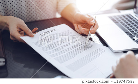 Business people sitting and discussing contract in office, closeup. Partners or lawyers working together at meeting before signing papers. Teamwork and partnership 119747582
