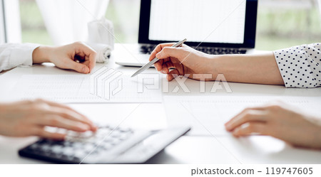 Two accountants using a calculator and laptop computer for counting taxes at white desk in office. Teamwork in business audit and finance 119747605