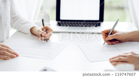 Two accountants using a laptop computer for counting taxes at white desk in office. Teamwork in business audit and finance Two accountants using a laptop computer for counting taxes at white desk in office. Teamwork in business audit and finance 119747607