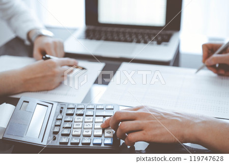 Two accountants use a calculator and laptop computer for counting taxes or revenue balance. Business, audit, and taxes concepts 119747628
