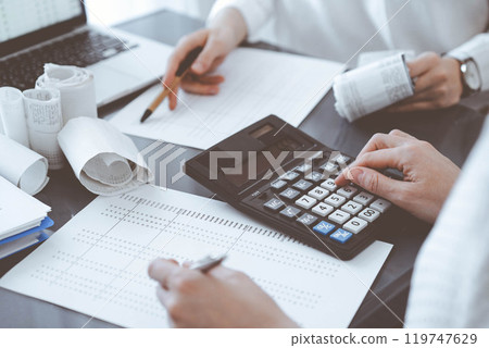 Two accountants use a calculator and laptop computer for counting taxes or revenue balance. Business, audit, and taxes concepts 119747629