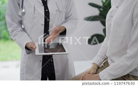 Doctor and a patient. The female physician is pointing into tablet computer besides a young woman during a consultation in the clinic, view above. Medicine concept Doctor and a patient. The female physician is pointing into tablet computer besides a young woman during a consultation in the clinic, view above. Medicine concept 119747630