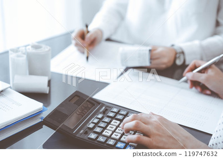 Two accountants use a calculator and laptop computer for counting taxes or revenue balance. Business, audit, and taxes concepts 119747632