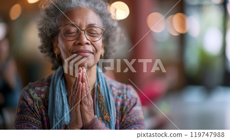 A mature woman peacefully reflects and prays in a cozy space surrounded by soft lighting in the late afternoon 119747988