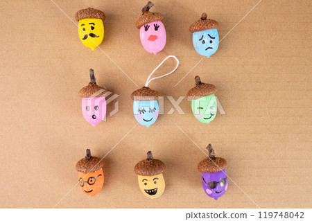 Painted acorns with expressive faces on brown background. Showcasing artistic crafting ideas, perfect for autumn designs, DIY concepts, and creative seasonal projects. 119748042
