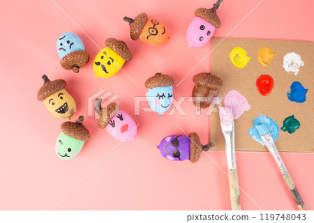 Colorful painted acorns next to a paint palette and brushes on a light pink background. Studio shot for craft projects and autumn decorations. DIY and creativity concept. Design for greeting card, 119748043