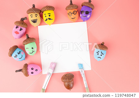 The acorns have brown caps and are painted in colors such as blue, yellow, orange, green, The facial expressions range from happy to sad. The blank white square in the center is empty 119748047