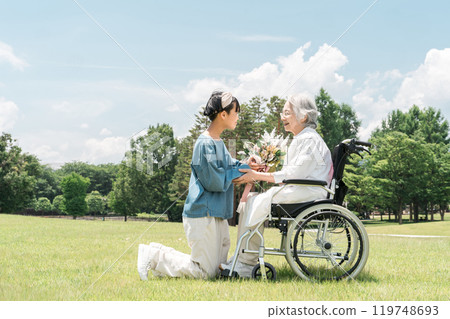 Smiling granddaughter presents a bouquet of flowers to her grandmother in a wheelchair 119748693