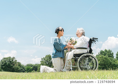 微笑的孫女向坐在輪椅上的祖母獻上一束鮮花 119748694