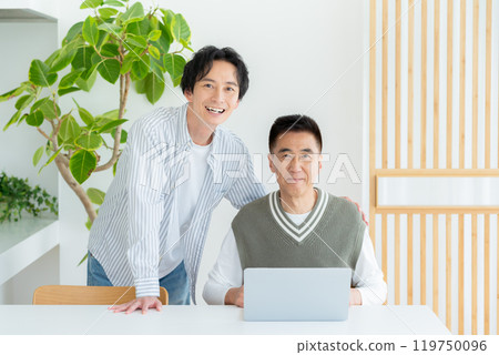 Senior man operating a computer in the living room 119750096