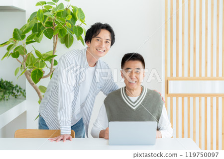Senior man operating a computer in the living room 119750097