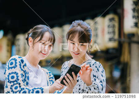 A woman looking at her smartphone with a friend while sightseeing in Osaka A woman looking at her smartphone with a friend while sightseeing in Osaka 119751098