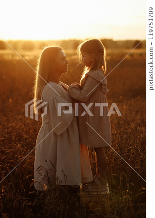 Woman and child standing in a field at sunset 119751709