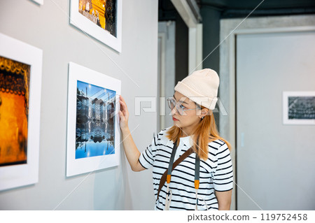 Asian woman hold camera at art gallery collection in front framed paintings pictures on wall and looking, Photographer visit at photo frame to leaning against at show exhibit artwork gallery picture 119752458