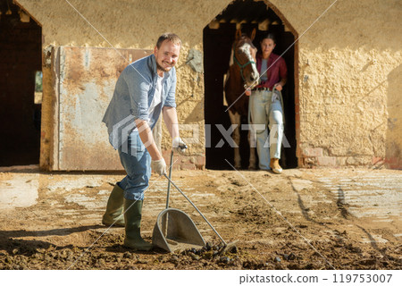 Young man cleans manure near stable 119753007