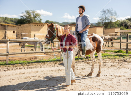 Young woman leading horse with man riding 119753059