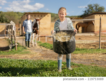 Boy with bucket of hay feed for horse Boy with bucket of hay feed for horse 119753089