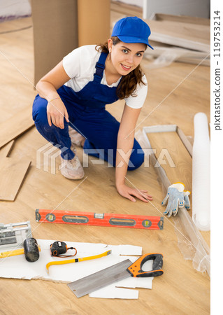 Repair in the room - woman puts laminate on the floor and checks horizontal level Repair in the room - woman puts laminate on the floor and checks horizontal level 119753214