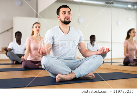 Man practising lotus pose with group in gym 119753235