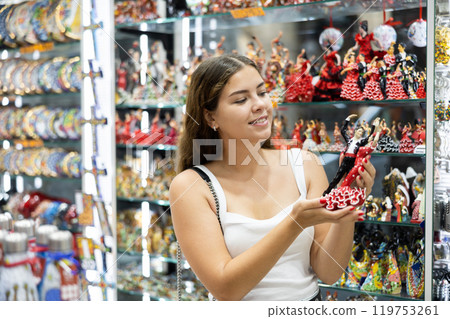 Interested young woman viewing Spanish dancer statuettes in souvenir store in Barcelona 119753261