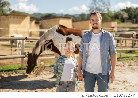 Portrait of happy father with his son on horse farm 119753277
