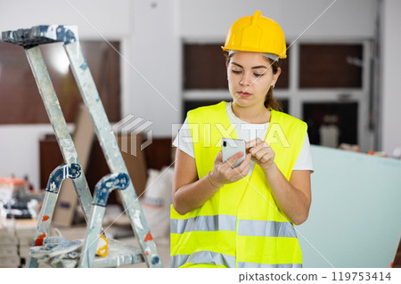 Focused female foreman using smartphone at construction site 119753414