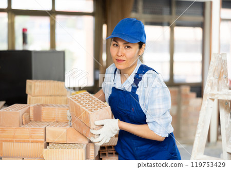 Female builder carrying hollow clay bricks and putting them on brick stack Female builder carrying hollow clay bricks and putting them on brick stack 119753429