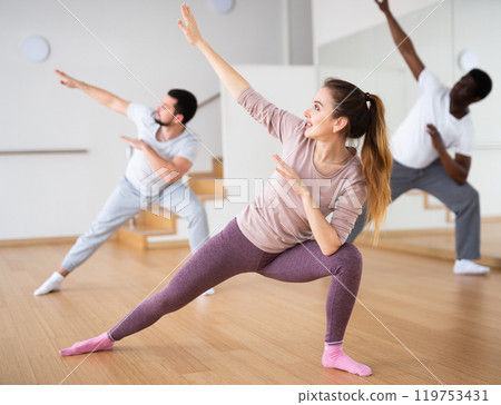 Young woman practicing vigorous dance movements with group 119753431