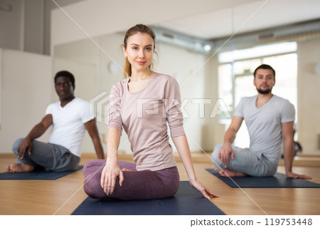 Woman practicing Parivritta Ardha Padmasana during group yoga training 119753448