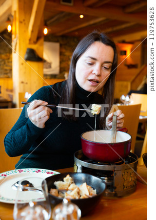 Woman having meal in Swiss restaurant, eating fondue 119753628