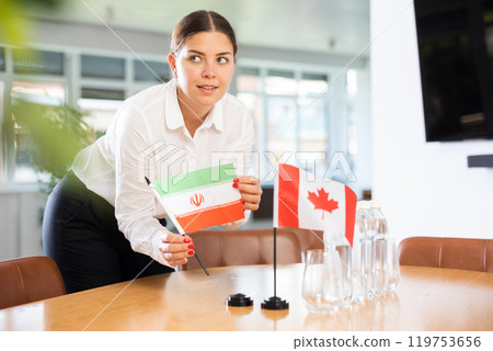 Young lady sets miniatures flags of Canada and Iran before international negotiations 119753656