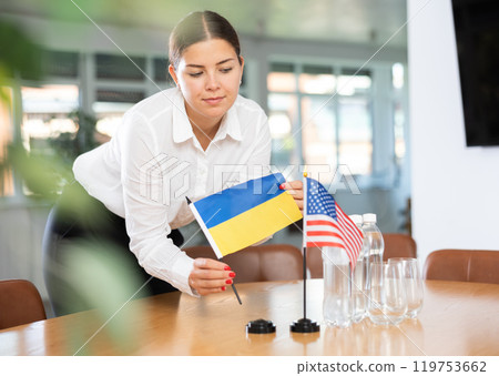 Female office coordinator placing flags of Ukraine and United States on table Female office coordinator placing flags of Ukraine and United States on table 119753662