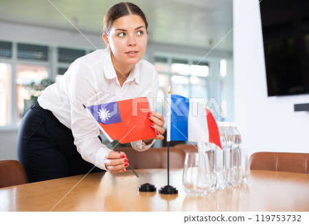 Woman secretary prepares an office for negotiations - she places flags of France and Taiwan table 119753732