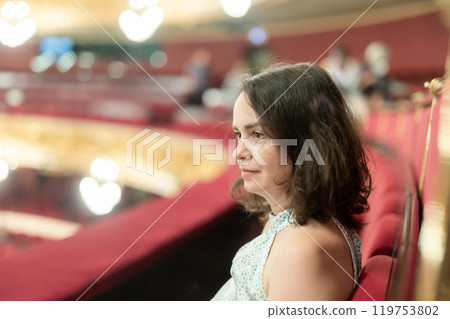 Girl visiting opera theater from upper floor of dress circle looks at stage and watches performance Girl visiting opera theater from upper floor of dress circle looks at stage and watches performance 119753802