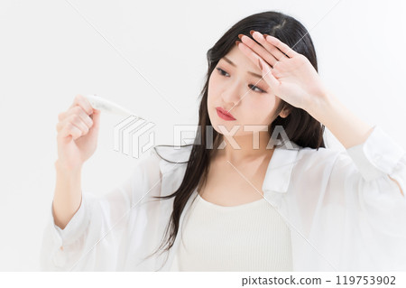 Young woman holding her hand on her forehead while looking at a thermometer 119753902