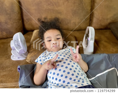 Portrait of cute Asian little girl on sofa with electric fan 119754299