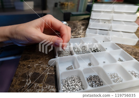 Top view artistic female hands creating bracelet from stones. POV shot of woman working with craft. Accessories on workshop table close up Top view artistic female hands creating bracelet from stones. POV shot of woman working with craft. Accessories on workshop table close up 119756035