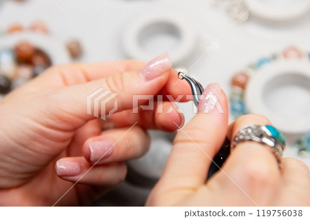 Woman creating custom jewelry. Macro shot of hands with pliers gripping a metal ring, jewelry making process, first person Woman creating custom jewelry. Macro shot of hands with pliers gripping a metal ring, jewelry making process, first person 119756038