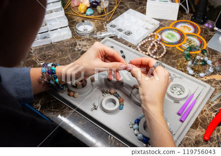 Caucasian woman assembles handmade jewelry bracelets made of stones and metal in her workshop with dark lighting and mysterious atmosphere 119756043