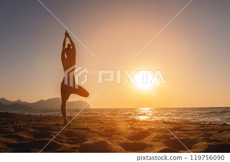 Vrikshasana tree pose from yoga, female silhouette at sunset or sunrise. Back view of a girl practicing morning workout on the seashore 119756090