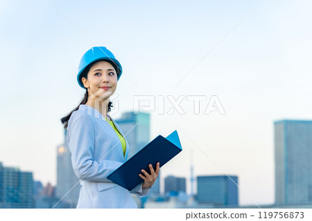A female designer and architect wearing a helmet and looking at the city 119756873