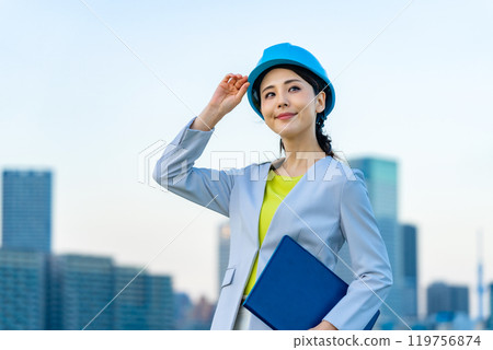 A female designer and architect wearing a helmet and looking at the city A female designer and architect wearing a helmet and looking at the city 119756874